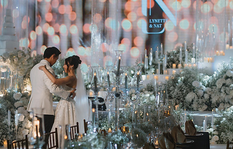 Bride and groom standing on a luxury hotel wedding stage with floral backdrop, candles, and grand staircase in Chiang Mai.