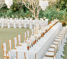"Outdoor wedding dinner setup in front of European villa, with long white table, wooden chairs