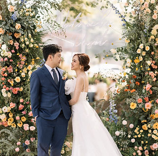Bride and groom standing under colorful floral arch in a romantic outdoor wedding ceremony