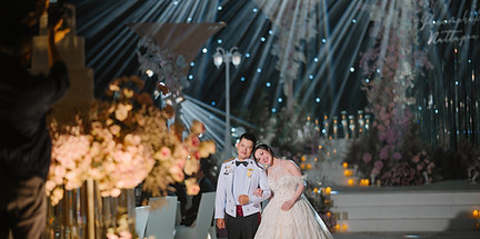 Bride in a long train gown standing with groom at a hotel wedding reception stage with spotlight
