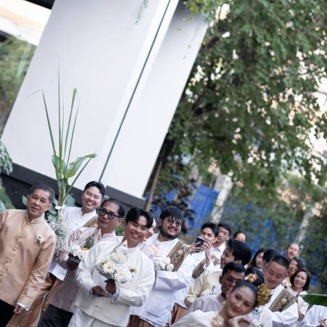 Joyful group photo of the bridal party, bridesmaids, and groomsmen in matching Thai contemporary attire.