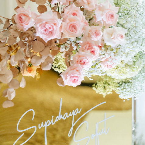 Close-up of a clear acrylic sign with gold calligraphy text, surrounded by pink and peach roses.