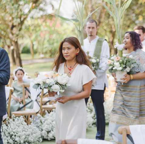 A bridesmaid in a white dress holding a delicate white floral arrangement.