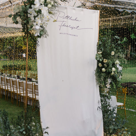 A minimalist white wedding welcome banner hanging in a garden setting.