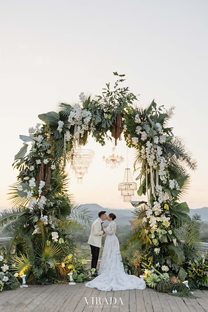 A stunning visual collection showcasing the picturesque outdoor destination wedding of Tania and Lionel. Set against a beautiful mountain backdrop, the reception features sophisticated white marquee tents, matching ivory tablescapes, and prominent sage green welcome boards. Key highlights include the couple's romantic kiss under a floral arch, bridesmaids in matching lime-green dresses, traditional hostesses in Thai silk wraps, and intricate local garlands decorating the venue.
Thoughtfully planned and designed by VIRADA Creative Wedding Planner, specializing in luxury destination weddings in Chiang Mai, Thailand.