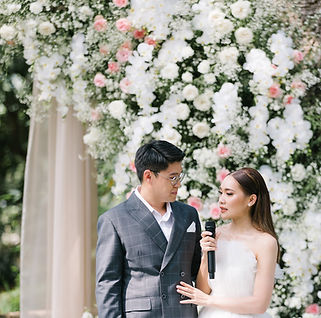 Bride and groom giving a speech during outdoor wedding ceremony with white and pink floral arch backdrop