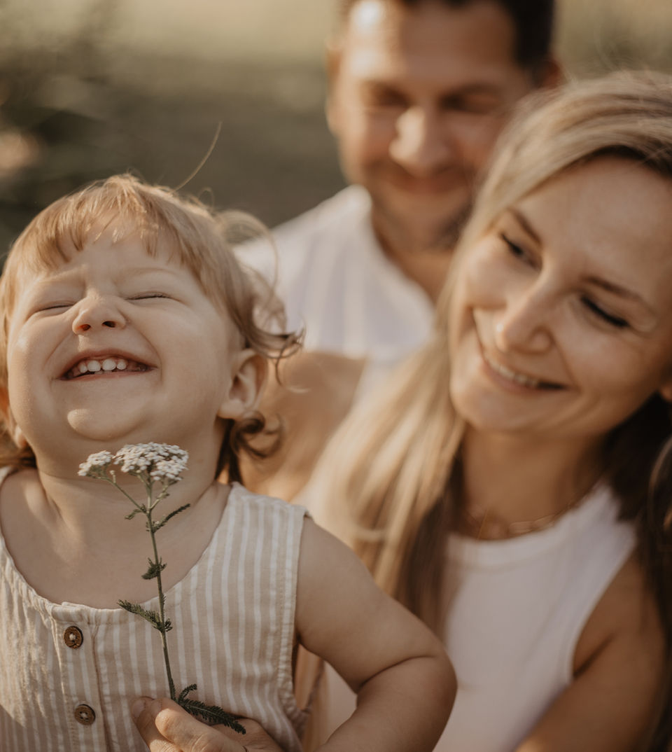 Kind wird mit Blume am Kinn gekitzelt und lacht herzhaft