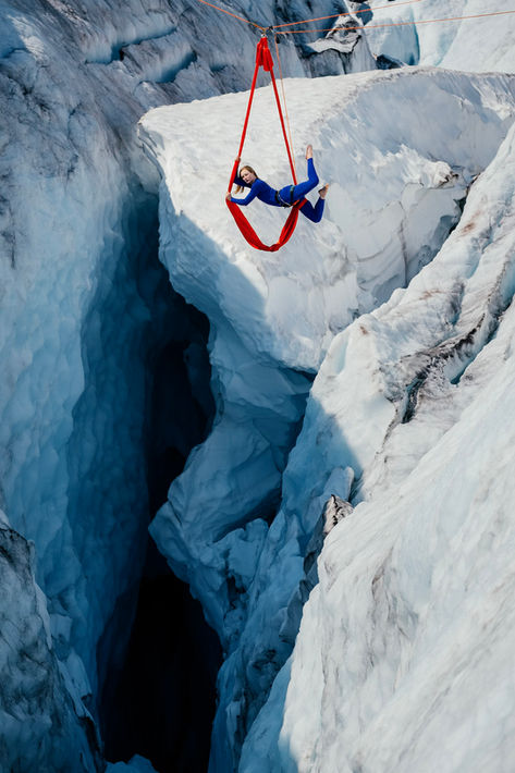 Sasha Galitzki, Aerialist, hosts position using red aerial silks against a crevasse. Book aerial performer for your corporate entertainment.