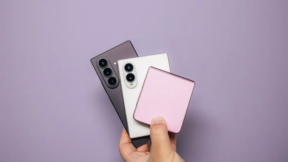 Hand holding three foldable smartphones Samsung Galaxy in black, white, and pink on a lavender background.