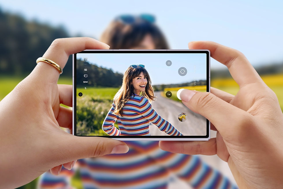 Hands hold a smartphone framing a smiling woman in a striped shirt on a sunny country road, with camera icons on screen.