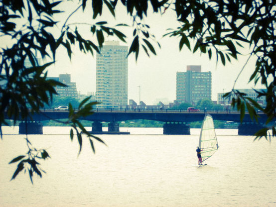 A parasailed on the Charles river. We see buildings rising in the background.