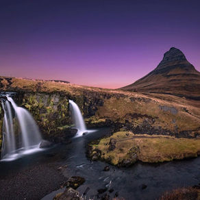 Kirkjufell mountain at sunset, reflecting in still water with nearby waterfall in foreground. Dramatic sky over Iceland’s iconic peak.