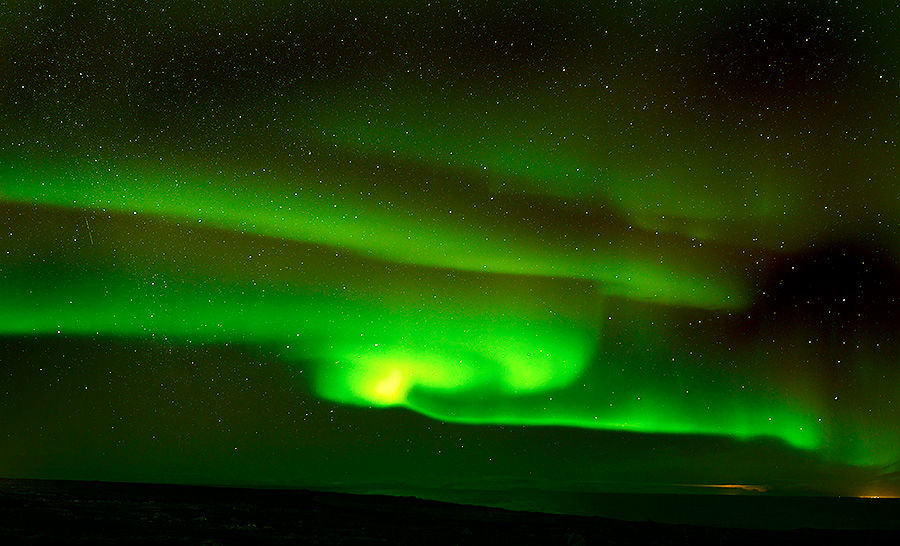 Green aurora borealis lights up a starry night sky over a dark landscape, creating a serene and mesmerizing natural display.