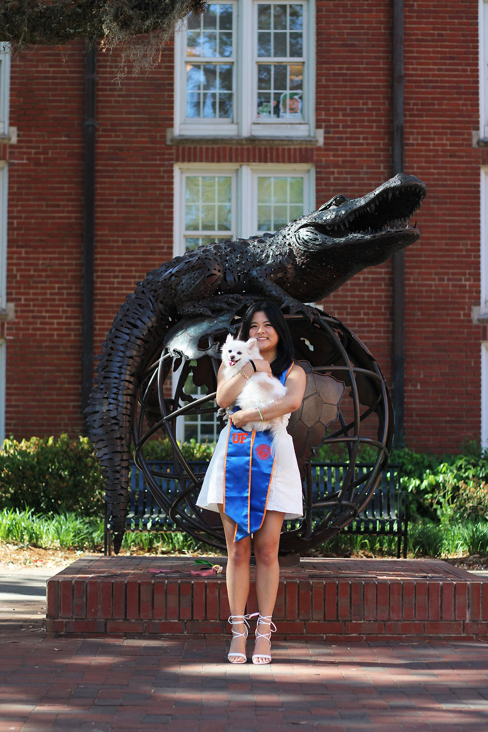 A graduate holding her dog in front of a university statue