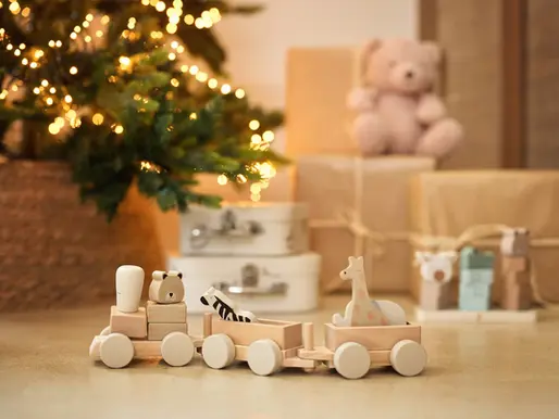 Holzeisenbahn mit Safari-Tieren aus FSC-Holz steht vor einem warm beleuchteten Weihnachtsbaum.