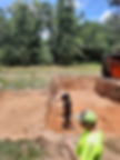 Workers excavating a deep rectangular pit in orange soil.