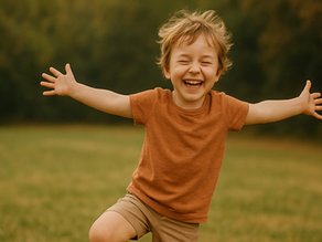 heart-filled photo of a child giggling, eyes scrunched in joy, standing in tree pose with arms wide open like branches. Their shirt is slightly crooked, their hair messy from play and they are completely radiant.