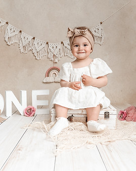 1 Geburtstagsshooting ein Mädchen sitzt auf einer Koffer und im hintergrund findet man neutrale dekoelemente zum 1 Geburtstag.