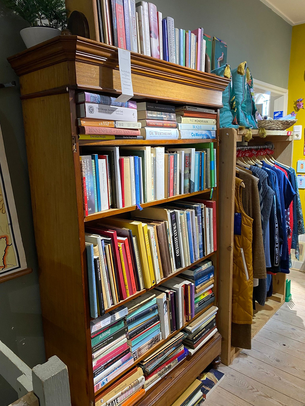 Hoge houten boekenkast vol boeken met een kledingrek ernaast