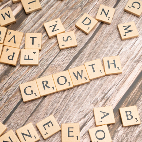 Scattered wooden letter tiles on a wooden surface spell "GROWTH" in the center. Other letters and words are incomplete.