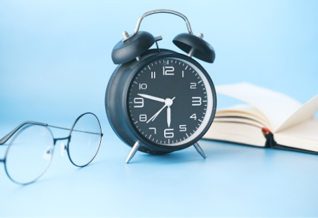 Black alarm clock shows 10:10 on a blue background, with open book and glasses nearby, creating a calm, studious mood.