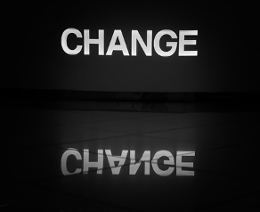 The word "CHANGE" is illuminated in white against a dark background, reflected clearly on a shiny surface, creating a contemplative mood.