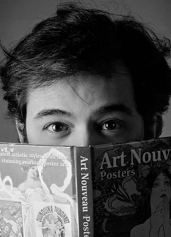 Imagem em preto e branco do autor e escritor Marcelo Nery em close-up segurando um livro de art nouveau aberto sobre o rosto.