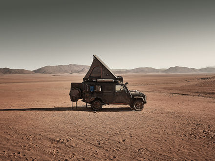 Overland Land Rover Defender with rooftop tent parked in a vast desert landscape, surrounded by open plains and distant mountains, capturing remote off-road travel and the spirit of long-distance adventure with Gravel & Salt.