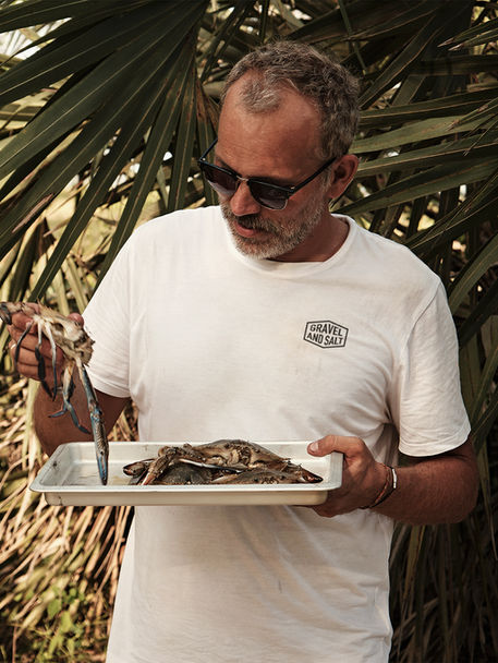 Gravel & Salt overlanding man holding fresh blue crabs for outdoor cooking.