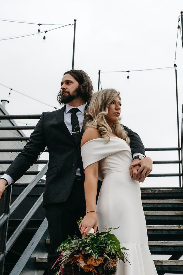 A wedding couple standing on stairs looking out into the distance.