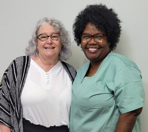 Two women with glasses smiling, one with gray hair, one with dark curly hair.