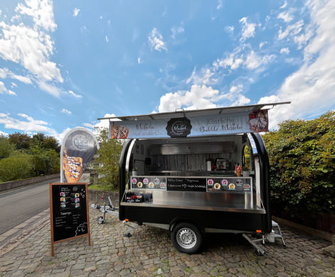 Man sieht den Wunderwaffelwagen komplett aufgebaut. Ein schwarzer Foodtruck mit einladenden Fahnen und
