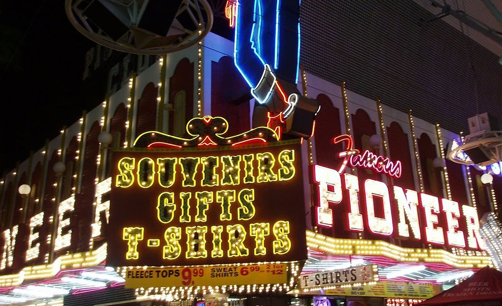 A bright hotel gift shop filled with shiny Vegas magnets, mugs, and T-shirts—attractive displays masking inflated prices compared to local stores.