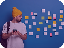 Man in a yellow beanie using a smartphone, standing in front of a wall covered with sticky notes, representing UX interaction and brainstorming.