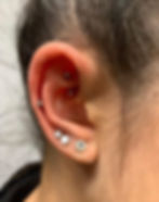 A close-up image of a freshly pierced ear with multiple piercings, including a rook piercing with a curved barbell, a helix piercing, and three lobe piercings adorned with clear gemstone studs. The ear appears slightly red, indicating recent piercing. This image highlights the importance of proper aftercare, as outlined in Xtremeties Tattoo & Piercing Studio’s guide on cleaning piercings to ensure proper healing. Located in Mississauga, Ontario, Xtremeties Tattoo & Piercing Studio offers professional piercing services with expert aftercare advice. For consultations, call (905) 897-3503 or visit our studio.