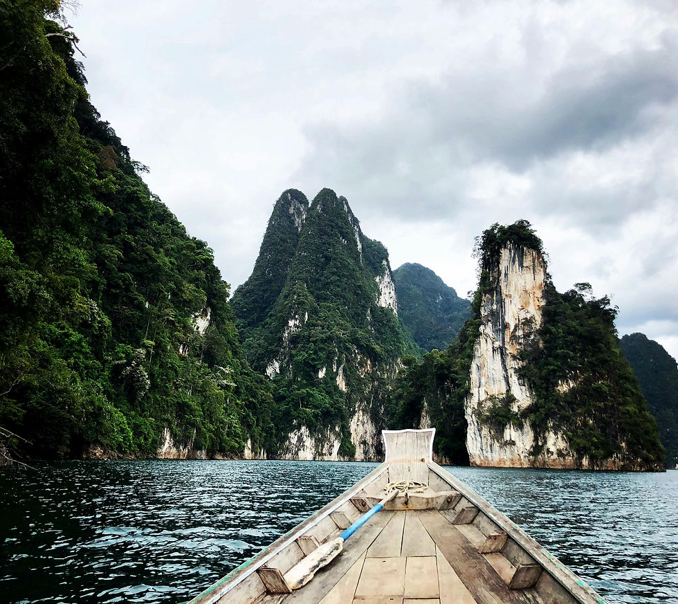 Boat on a serene lake surrounded by towering green limestone cliffs, under a cloudy sky, conveying a peaceful, natural setting in Khao Sok National Park.