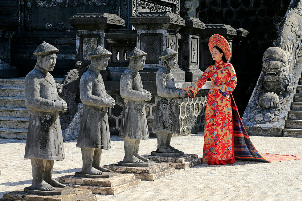 A woman in thai traditional dress stands among weathered stone statues, reaching out to touch one in Nong Khai. Historical, serene setting.