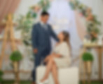 Couple in formal attire in front of floral arch and LOVE sign