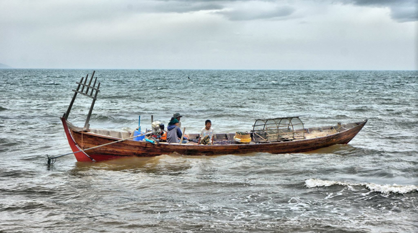 A wooden boat loaded with woven crab traps heads back to shore, under a low, cloud-heavy sky