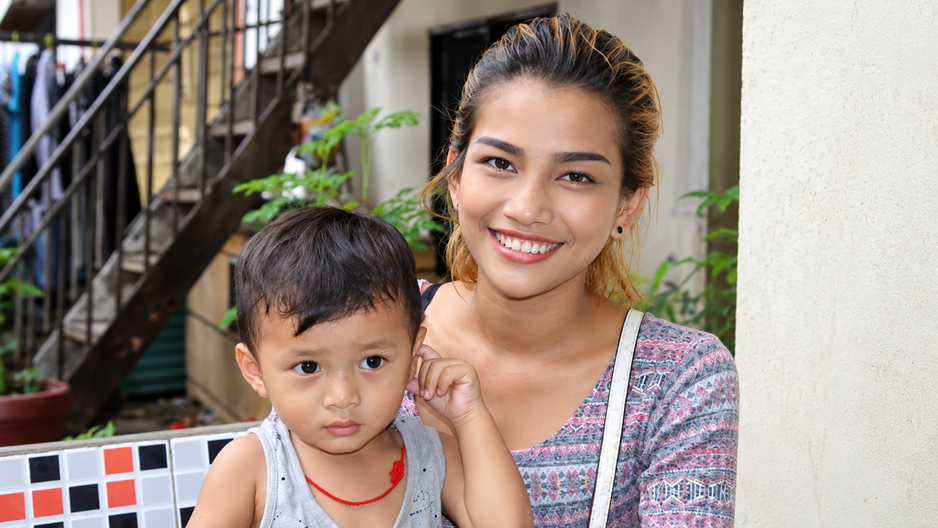 A young woman smiles. The child she holds against her looks serious