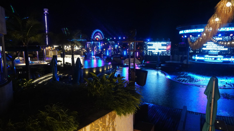 e Khayangan Beach Club un samedi soir de pluie : bassins éclairés, écran LED, scène et, au loin, la grande roue