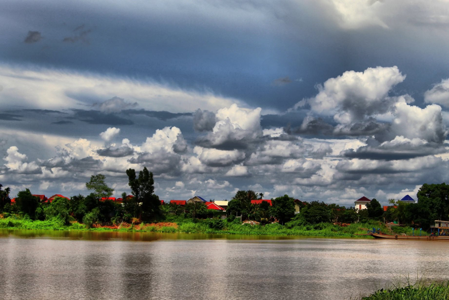 De lourds nuages d'orage roulent au-dessus du Bassac, couleur de terre battue, tandis que la rivière glisse devant les toits rouges du village en face de l’île