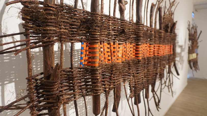A woven panel combining forest vines with orange and blue industrial strapping