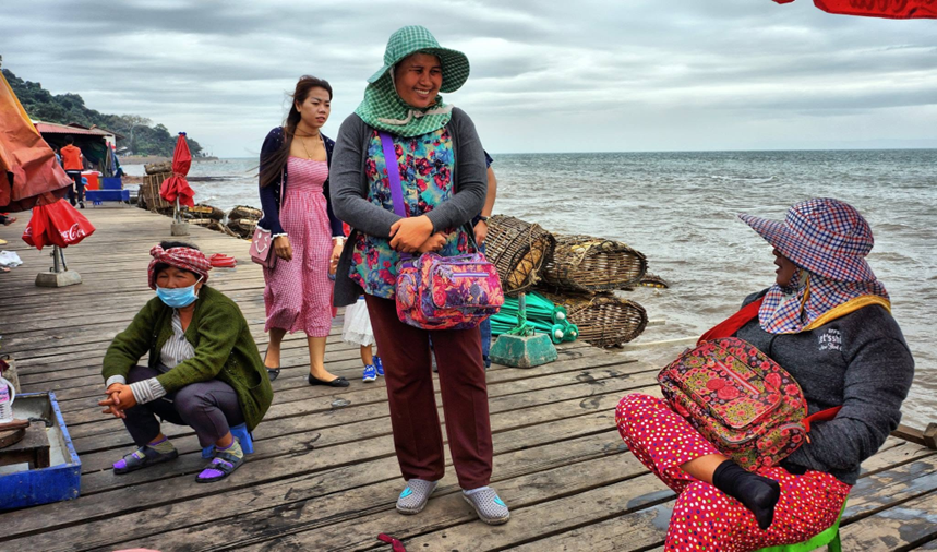 On the market pier, a beaming vendor poses among her neighbours, not far from the woven baskets stacked at the water's edge