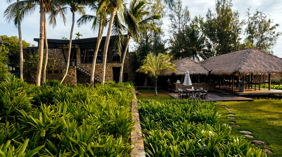 Thatched pavilions and stone architecture at dusk, framed by coconut palms
