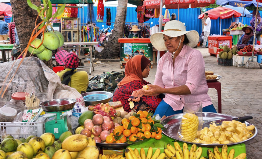 Near the market, a vendor peels fruit for a veiled customer, amid a stall piled high with mangoes, mangosteens, dragon fruit and freshly cut jackfruit