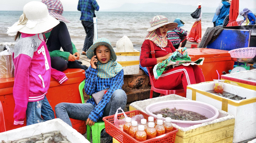 On the market pier, vendors take a quiet moment, surrounded by coolers, bottles of chilli sauce and a tub of fresh shrimp