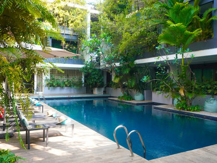 Il existe des adresses que l'on pressent singulières bien avant d'y poser ses bagages. Anjali by Syphon est de celles-là. Posée sur la Korean-Cambodian Friendship Road, à quelques minutes seulement des temples d'Angkor, cette maison de caractère se révèle, dès les premières secondes, comme un refuge hors du temps — une coulée de verdure au cœur d'une ville en pleine effervescence.