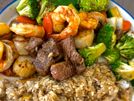 Plate of shrimp, beef, broccoli, and fried rice, colorful and glossy on a white-rimmed dish.