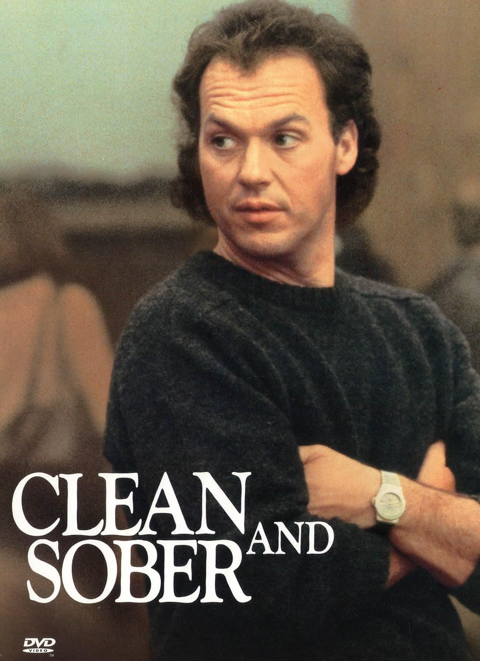 Man in dark sweater looks to the side with crossed arms, exuding a serious mood. Text reads "Clean and Sober." Background is blurred.
